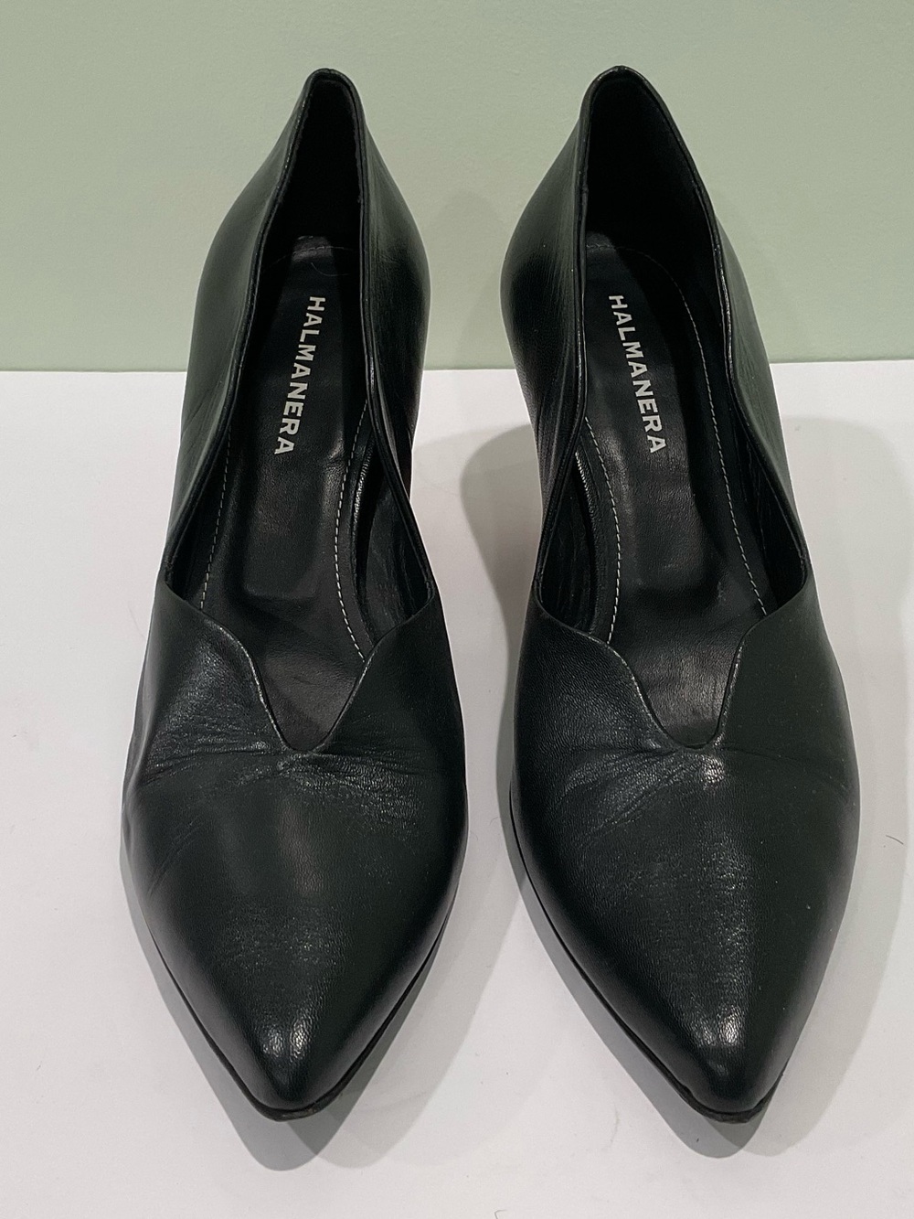 Black leather pointed-toe slip-on pumps by Halmanera featuring a distinct V-cut.